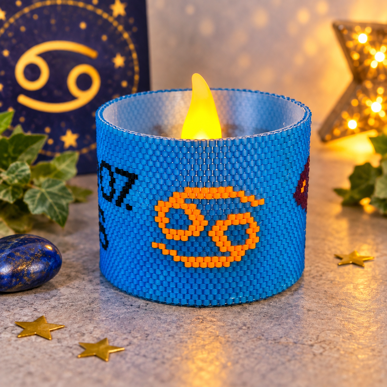 Windlichtumrandung Krebs aus blauen Perlen mit orangefarbenem Sternzeichen-Symbol und leuchtendem LED-Teelicht